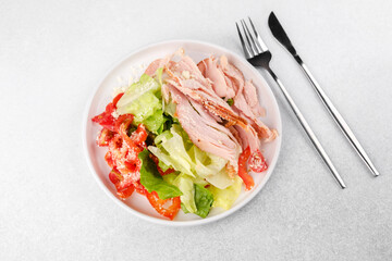 Protein salad with turkey, cheese and vegetables in white bowl with cutlery for fitness meal plan or diet food concept
