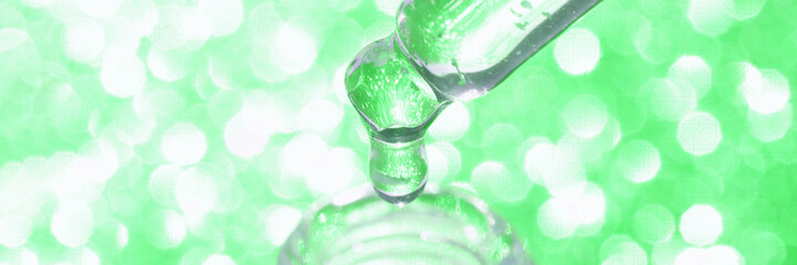 Close-up of dropping liquid serum from dropper against bright green bokeh background.