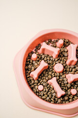 Pink dog bowl with bone shapes holding dry pet food on a plain background