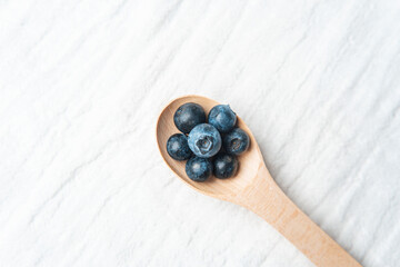 Fresh blueberries arranged in a wooden spoon on a light background