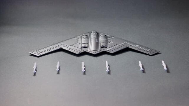 Top view of B2 spirit stealth bomber scale model displayed on a blue surface with five missiles arranged below. The iconic flying wing design represents modern aviation, stealth technology