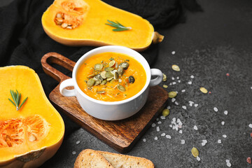 Hot pumpkin soup in white bowl with seeds and rosemary, garnished with bread