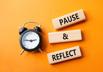 Pause and Reflect symbol. Concept words Pause and Reflect on wooden blocks. Beautiful orange background with alarm clock. Business and Pause and Reflect concept. Copy space.