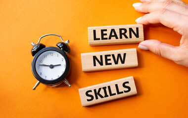 Learn new skills symbol. Concept words Learn new skills on wooden blocks. Businessman hand. Beautiful orange background with alarm clock. Business and Learn new skills concept. Copy space.