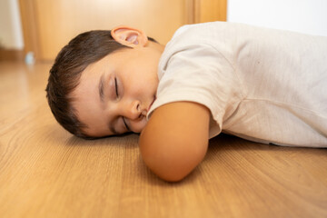 Child sleeping on wooden floor. Funny tired little boy falling asleep crawling on hardwood floor at home.