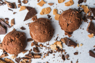 Three scoops of chocolate ice cream surrounded by broken waffle cones and chocolate chunks on light surface