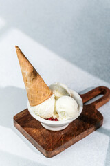 Vanilla ice cream scoops in bowl with cone on wooden board in sunlight