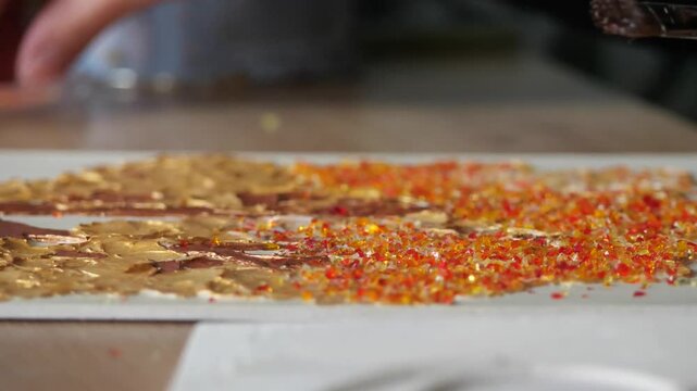 A hand sprinkles fine red glass crumbs or sand onto a colorful glass art project - An artist's fingers gently press small, colorful glass pieces into wet glue on an MDF board