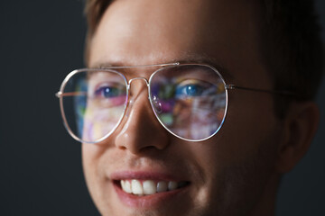Fototapeta premium Smiling man wearing glasses with reflection on dark background, closeup