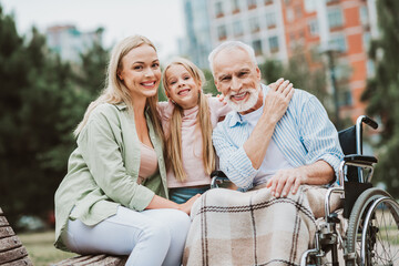 Heartwarming family moment in the park as grandpa in a wheelchair shares smiles with daughter and granddaughter and shows love and care