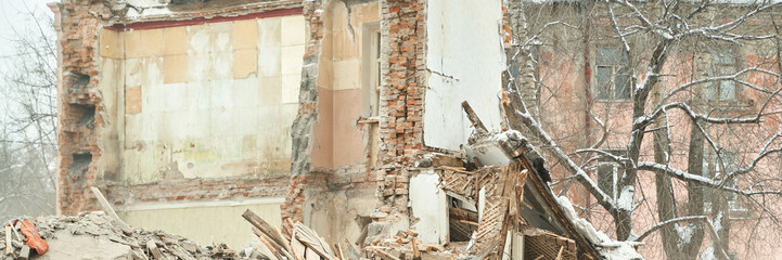 Partial demolition of brick building in winter urban landscape with snowy trees and exposed walls.