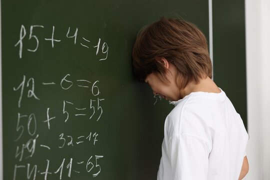 Back to school. Upset boy near chalkboard with math assignment indoors - Powered by Adobe