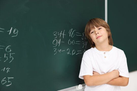 Back to school. Boy near chalkboard with math assignment indoors