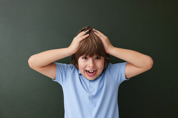 Back to school. Emotional boy near green chalkboard indoors