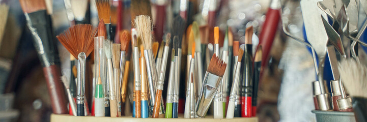 Assorted paintbrushes in a holder displaying various shapes and sizes in an artists studio.