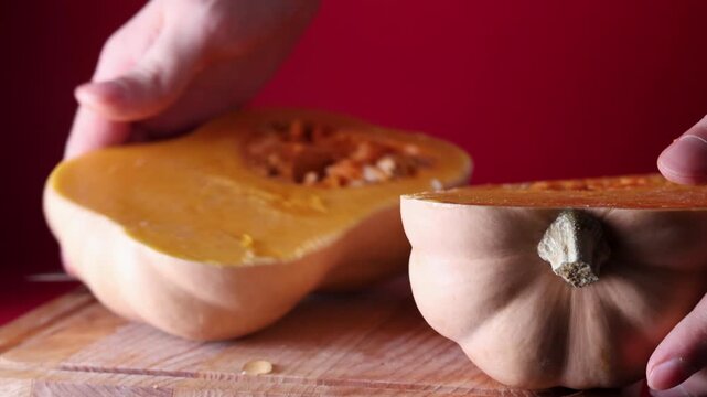 Close-up view of a person splitting a butternut squash in half by hand after making an initial cut. The action reveals the fresh orange flesh and natural texture of the vegetable