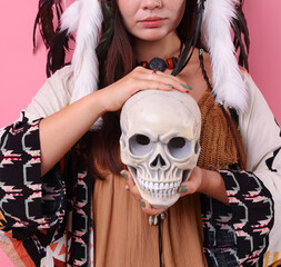 Shaman woman in native American Indian headdress with skull on pink background, closeup