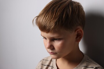 Upset little boy crying near light grey wall indoors, space for text