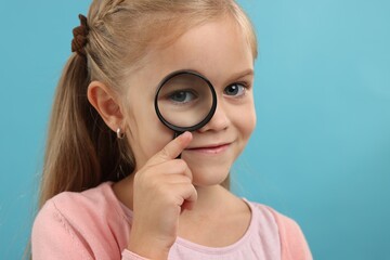 Little girl with magnifying glass on light blue background