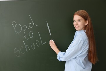 Girl writing phrase Back To School on chalkboard indoors