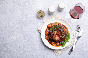 Tasty beef ossobuco with carrot, mushrooms and herbs served on grey textured table, flat lay. Space for text