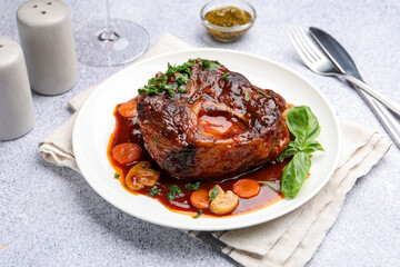 Tasty beef ossobuco with carrot, mushrooms and herbs on grey textured table, closeup