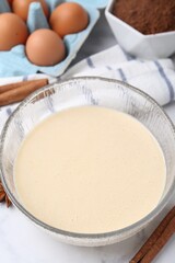 Liquid dough in bowl and ingredients on white table, closeup