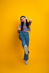 Energetic young woman with blue headphones dancing and pointing at the camera against a bright...