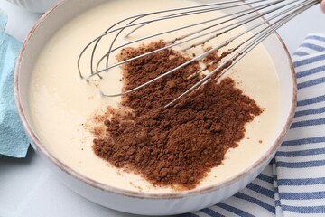 Adding cocoa powder into bowl with dough at white table, closeup