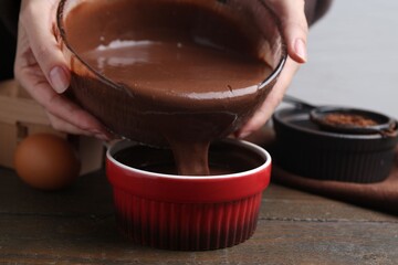 Woman pouring liquid chocolate dough into baking dish at wooden table, closeup