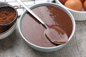Liquid chocolate dough in bowl and ingredients on grey table, closeup