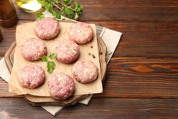 Raw meat patties with parsley and peppercorns on wooden table. Space for text
