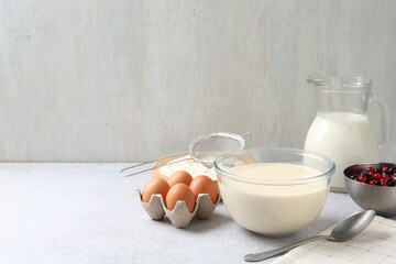 Liquid dough in bowl, berries and ingredients on light grey table, space for text