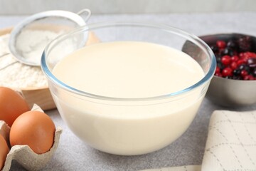 Liquid dough in bowl, berries and ingredients on light grey table, closeup