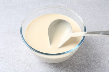 Taking liquid dough from bowl with ladle on light grey table, closeup