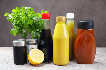 Bottles of different tasty sauces and products on grey table, closeup