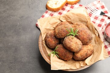Delicious patties with rosemary in bowl on grey textured table, closeup. Space for text