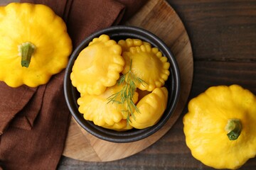 Pickled pattypan squashes in bowl and fresh vegetables on wooden table, flat lay