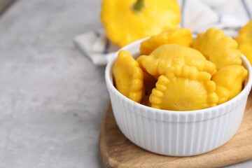 Pickled pattypan squashes in bowl on light grey table, closeup. Space for text