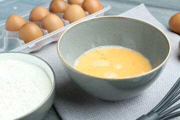 Beaten eggs in bowl, whisk and flour on table, closeup