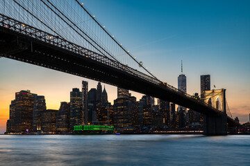 Fototapeta premium A beautiful view of the Brooklyn Bridge spanning the water, with the downtown Manhattan skyline and the Financial District illuminated at twilight.
