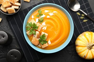 Tasty pumpkin cream soup with parsley and croutons served on dark textured table, flat lay