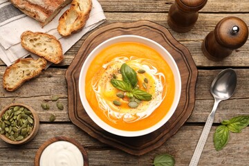 Delicious pumpkin cream soup with basil and seeds served on wooden table, flat lay