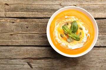 Delicious pumpkin cream soup with basil and seeds served on wooden table, top view. Space for text