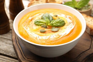 Delicious pumpkin cream soup with basil and seeds served on wooden table, closeup