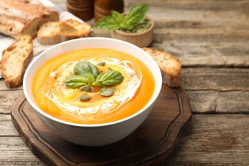 Delicious pumpkin cream soup with basil and seeds served on wooden table, closeup