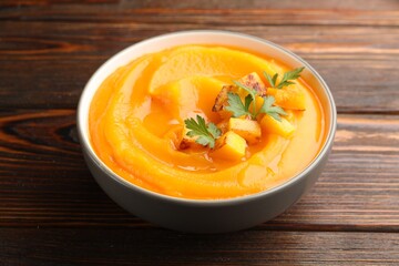 Delicious pumpkin cream soup with parsley served on wooden table, closeup