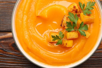 Delicious pumpkin cream soup with parsley served on wooden table, top view