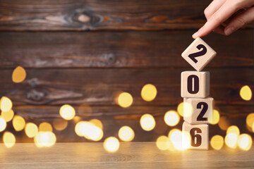 New 2026 Year. Woman putting cube with number 2 onto others on table, closeup
