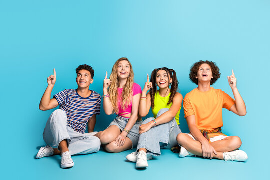 Fun bright teens group shot four friends point up smiling and enjoying a sunny blue background moment